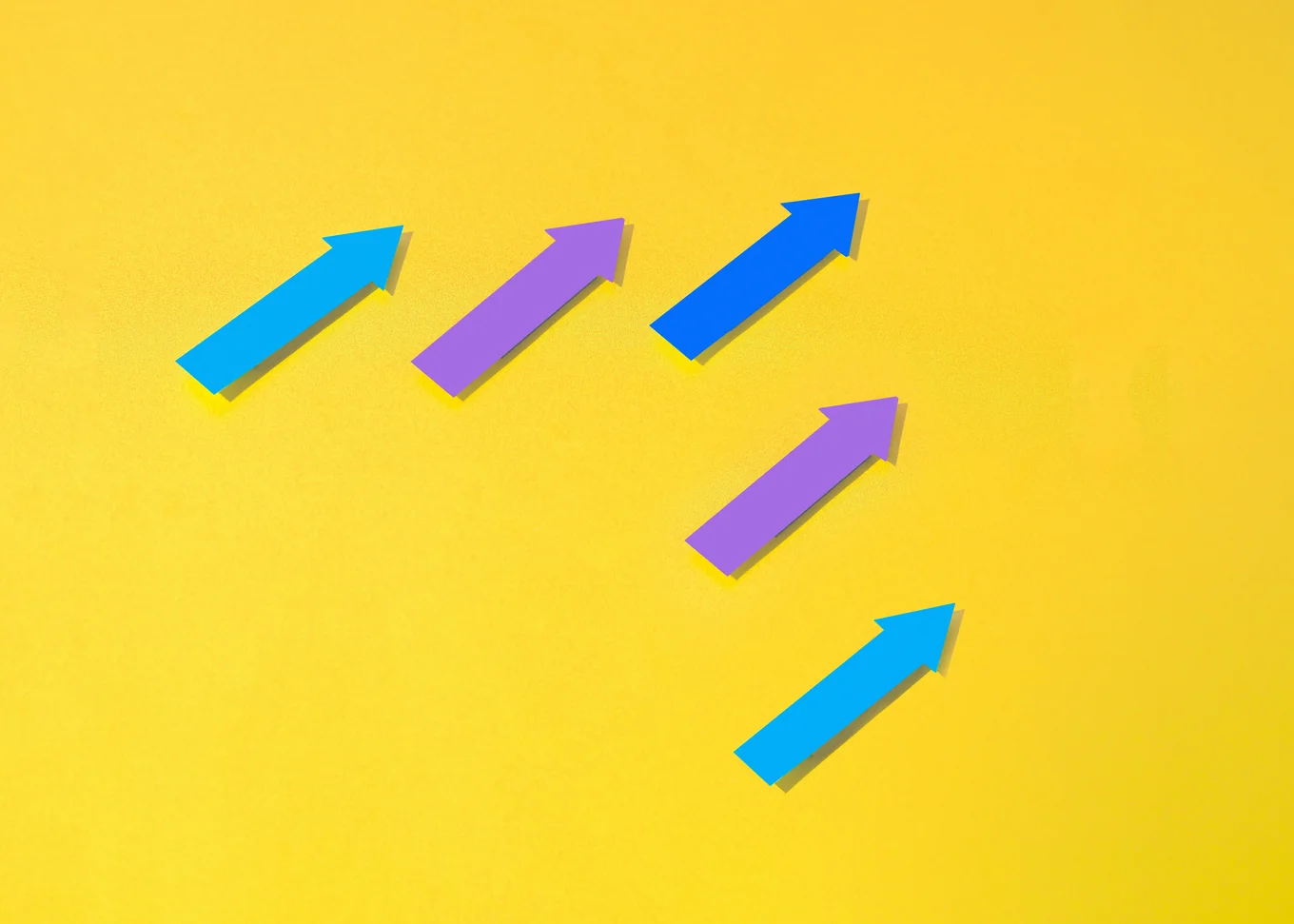 Five arrows, two purple and three blue, pointing toward the top right corner against a yellow background.
